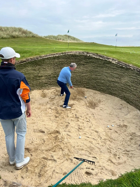 Der Coach macht`s vor, wie man den Ball aus einem tiefen Pottbunker schlägt.